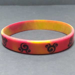 Op de afbeelding: Een rood en geel siliconen armband met een zwart swirl-ontwerp.