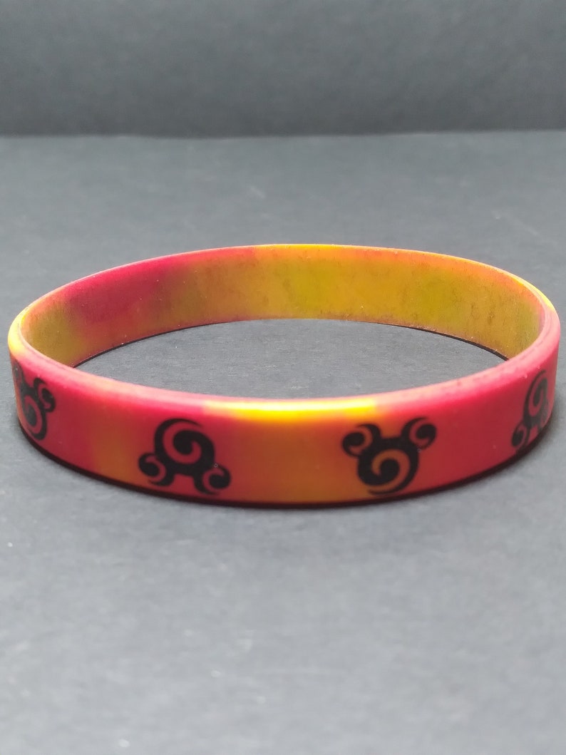 Op de afbeelding: Een rood en geel siliconen armband met een zwart swirl-ontwerp.