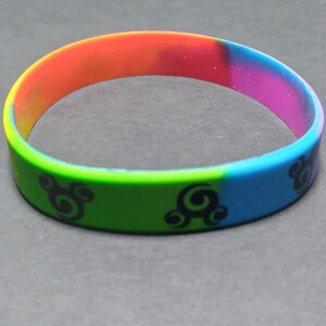 Op de afbeelding: Een veelkleurig siliconen armband met een zwart swirl-ontwerp. De armband is rood, oranje, geel, groen, blauw en paars.