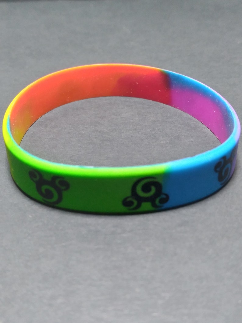 Op de afbeelding: Een veelkleurig siliconen armband met een zwart swirl-ontwerp. De armband is rood, oranje, geel, groen, blauw en paars.