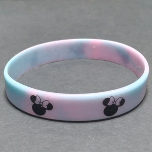May include: A pink and blue silicone bracelet with black Mickey Mouse ears and a bow on each side.