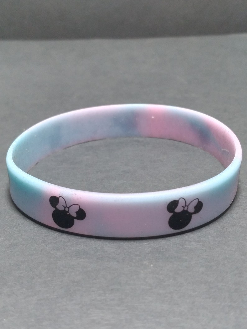 May include: A pink and blue silicone bracelet with black Mickey Mouse ears and a bow on each side.