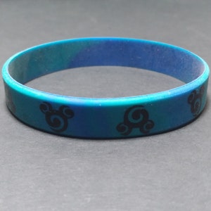 Op de afbeelding: Een blauwe en groene siliconen armband met een zwart swirl-ontwerp.