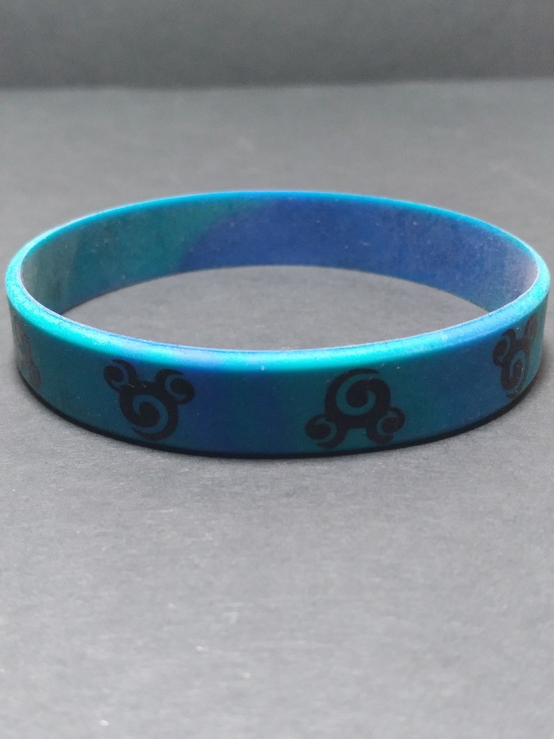Op de afbeelding: Een blauwe en groene siliconen armband met een zwart swirl-ontwerp.