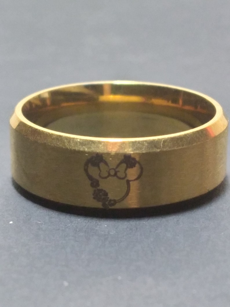 May include: A gold-colored ring with a Mickey Mouse silhouette engraved on the band.