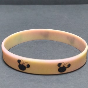 May include: A yellow and pink silicone bracelet with two black and white Mickey Mouse silhouettes.