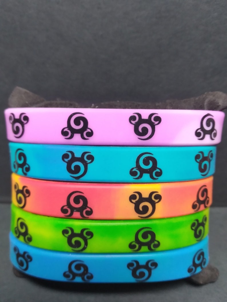 Op de afbeelding: Een stapel van vijf kleurrijke siliconen armbanden met een zwart swirl-ontwerp. De armbanden zijn in tinten roze, blauw, oranje, groen en lichtblauw.