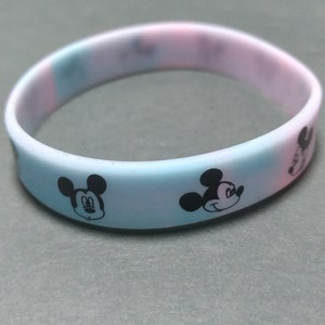 Puede incluir: Pulsera de silicona en colores pastel con motivos repetidos de la cara de Mickey Mouse en negro. La pulsera presenta un degradado de color de azul claro a rosa. Un divertido accesorio para los fans de Disney. Circunferencia de unos 19 cm.