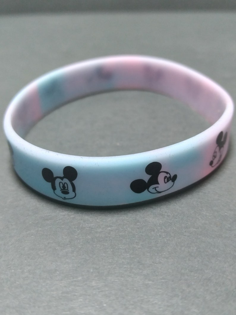 Puede incluir: Pulsera de silicona en colores pastel con motivos repetidos de la cara de Mickey Mouse en negro. La pulsera presenta un degradado de color de azul claro a rosa. Un divertido accesorio para los fans de Disney. Circunferencia de unos 19 cm.