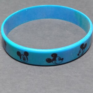 Puede incluir: Una pulsera de silicona azul con un patr&oacute;n repetido de la cara de Mickey Mouse.