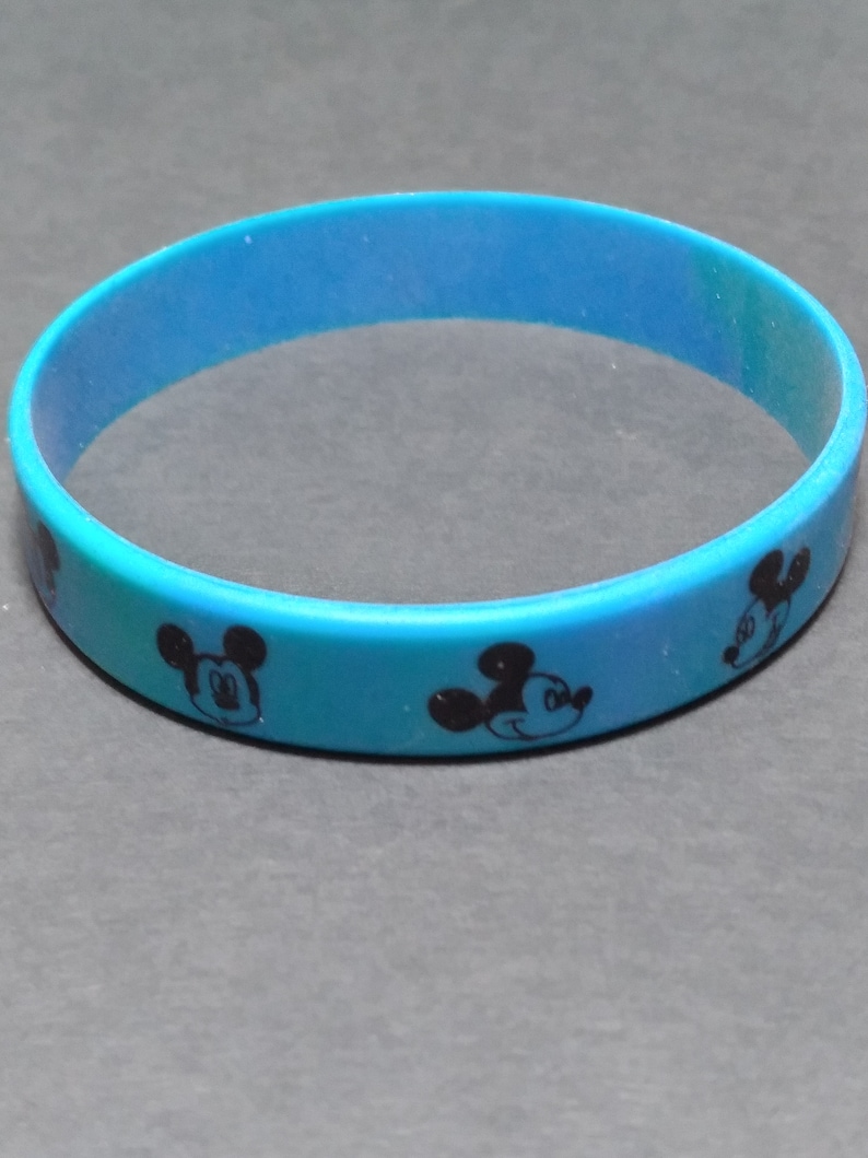 Puede incluir: Una pulsera de silicona azul con un patr&oacute;n repetido de la cara de Mickey Mouse.