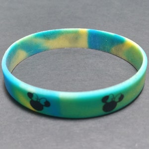 May include: A blue, yellow, and green silicone bracelet with a black silhouette of Mickey Mouse's head on each side.