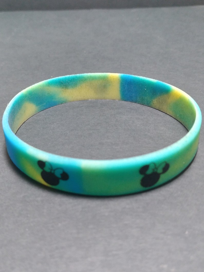 May include: A blue, yellow, and green silicone bracelet with a black silhouette of Mickey Mouse's head on each side.