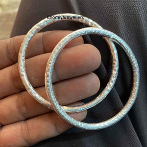 Könnte beinhalten: Zwei silberne Armreifen mit gehämmerter Textur. Die Armreifen liegen übereinander.