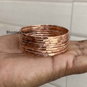 Peut inclure: Un ensemble de huit bracelets en cuivre martelé. Les bracelets sont empilés les uns sur les autres et sont d'une couleur chaude dorée rosée.
