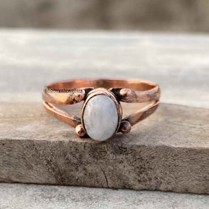 Può includere: Un anello in rame con una pietra di luna ovale bianca. L'anello ha un design delicato con piccoli accenti sulla fascia.