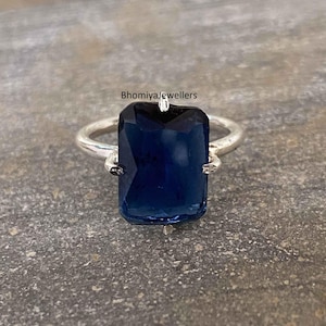 Può includere: Un anello d'argento con una grande pietra preziosa blu scuro di taglio smeraldo.