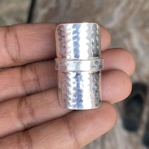 Peut inclure: Une bague en métal martelé argentée avec une large bande. La bague est composée de deux pièces superposées.