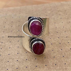 May include: A silver ring with two oval-shaped red gemstones set in a twisted band. The ring is decorated with a rope-like design around the gemstones.