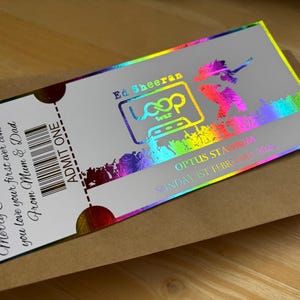 May include: A holographic Ed Sheeran concert ticket with rainbow detailing. The ticket, reading "ADMIT ONE", is for the Loop Tour and includes the concert date. It is presented on a brown envelope with a handwritten message.