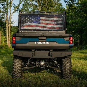 May include: A black Polaris off-road vehicle with a blue stripe and a distressed American flag displayed on the back.