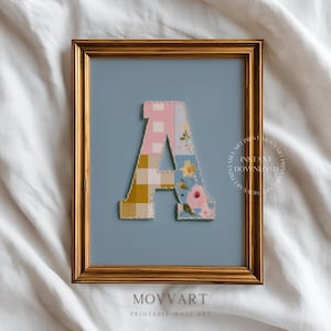 May include: Framed wall art featuring a patchwork letter "A" in pink gingham, yellow plaid, floral, and blue patterns. The gold frame surrounds a light blue background. The text "MOVART PRINTABLE WALL ART" is at the bottom.