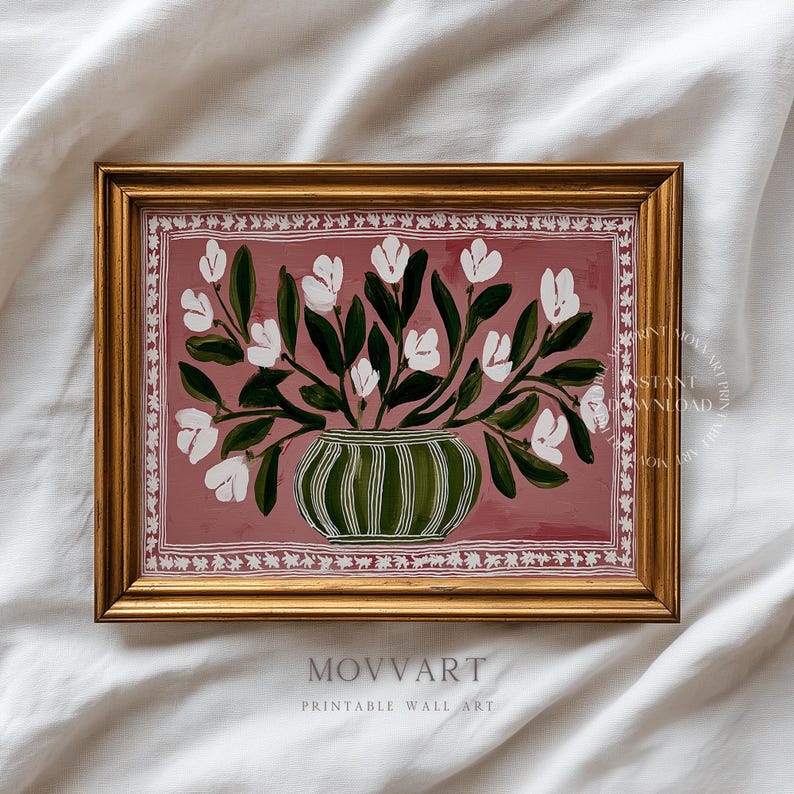 May include: A framed print featuring a floral still life. White flowers and green leaves are arranged in a green and white striped vase against a dusty rose background. The frame is gold, and the print includes the text "MOVART PRINTABLE WALL ART."
