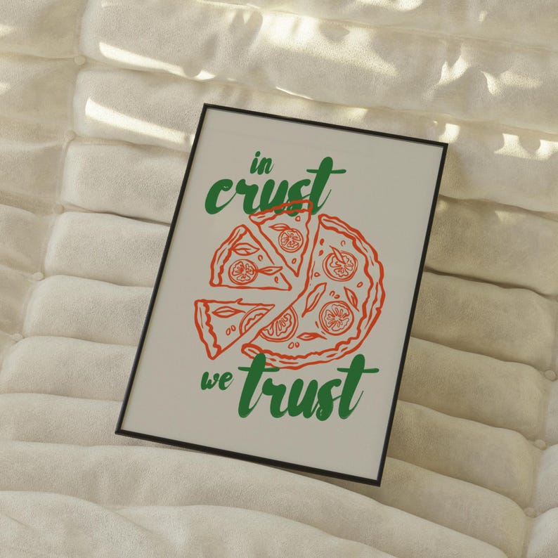 以下が含まれることがあります： 白い額縁に入ったプリントで、緑と赤の文字で「in crust we trust」と書かれています。プリントの中央には、赤とオレンジのピザの切り身が描かれています。
