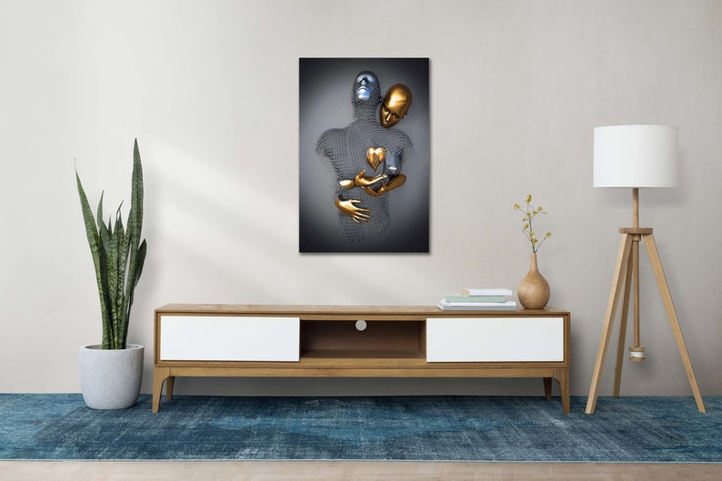 May include: Abstract metal sculpture of two figures embracing, one silver and one gold, with a gold heart in the center. The sculpture is displayed on a white wall above a wooden entertainment center.