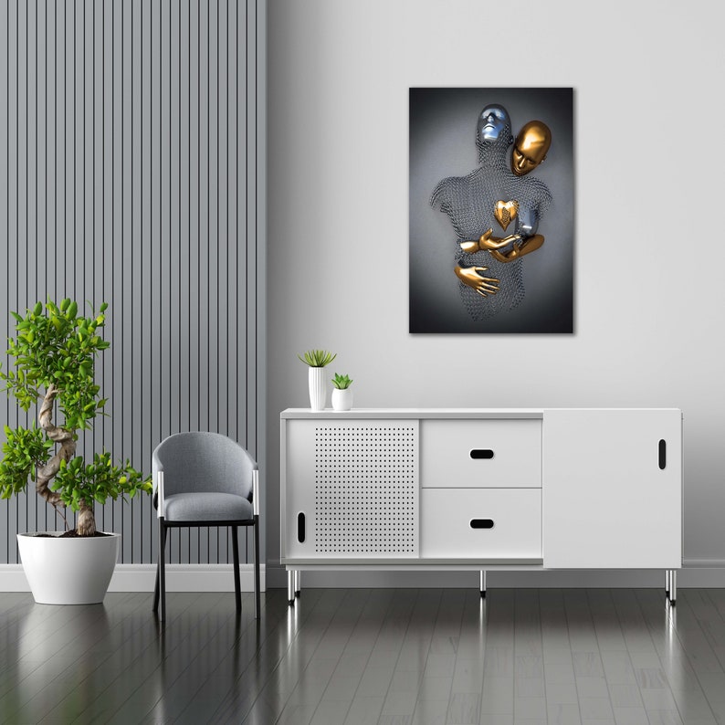 May include: Abstract metal sculpture of two figures embracing, one gold and one silver, with a gold heart in the center. The sculpture is displayed on a white wall above a white cabinet with a sliding door.