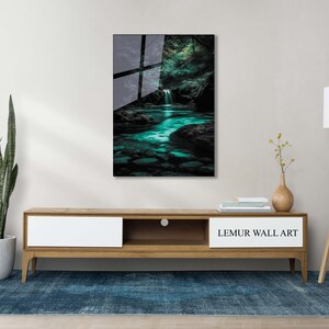 May include: A framed wall art print featuring a serene waterfall scene with turquoise water and dark rocks. The artwork is displayed above a wooden cabinet with a plant, lamp, and rug. The text "LEMUR WALL ART" is visible on the cabinet.