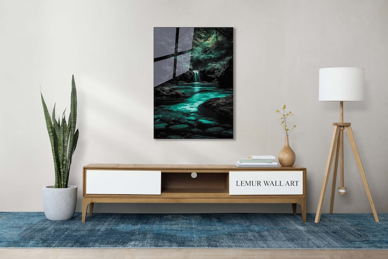 May include: A framed wall art print featuring a serene waterfall scene with turquoise water and dark rocks. The artwork is displayed above a wooden cabinet with a plant, lamp, and rug. The text "LEMUR WALL ART" is visible on the cabinet.