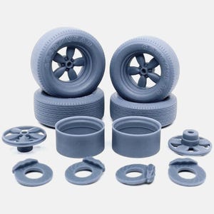 May include: A collection of gray model car parts, including tires with "Goodyear" text, wheels, brake components, and cylinders. The tires are stacked, and the other parts are arranged below.