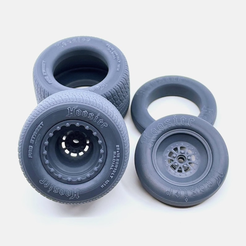 May include: Four gray Hoosier brand model car tires. Two tires have a black rim and the text "Hoosier" and "Pro Street" printed on the side. The other two tires are plain with the text "Hoosier" printed on the side.
