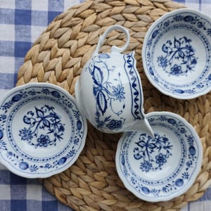 Puede incluir: Una taza de cerámica blanca con un asa negra y el texto "But First, Coffee" en negrita negra. La taza se encuentra sobre un fondo neutro, resaltando su diseño sencillo.