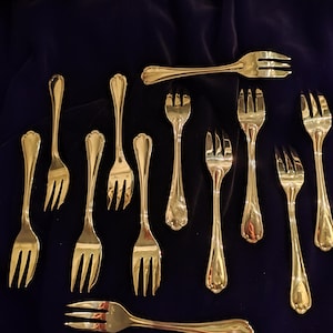 Op de afbeelding: Een assortiment glanzende, zilverkleurige vorken gerangschikt op een donkerblauwe fluwelen ondergrond. De vorken hebben een klassiek ontwerp met drie tanden en decoratieve handvatten. Een vintage bestekset.
