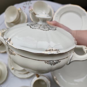 Könnte beinhalten: Cremefarbene Porzellan-Servierschüssel mit Deckel, Goldrand und dekorativen Akzenten. Teil eines Vintage-Teeservices, mit passenden Untertassen, Tassen und einem Sahnekännchen. Das Set hat ein klassisches, elegantes Design.