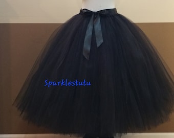 May include: A black tulle skirt with a black satin ribbon tie. The skirt is full and flowing, and the ribbon is tied in a bow at the back. The skirt is on a mannequin, and the text "sparklestutu" is visible on the skirt.