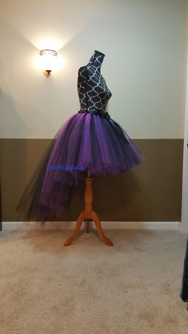 Puede incluir: Una falda de tul de color morado y negro con una cinta negra en la cintura. La falda es de estilo alto-bajo, con un frente m&aacute;s corto y una espalda m&aacute;s larga.