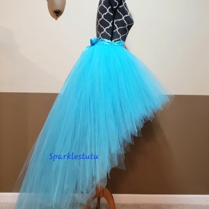 Puede incluir: Una falda de tul turquesa de corte alto-bajo con una cinta de raso en la cintura. La falda est&aacute; en un maniqu&iacute; y la falda es larga en la parte posterior y corta en la parte delantera.