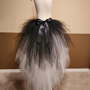 May include: A black and white tulle skirt with a satin bow. The skirt is displayed on a mannequin. The top layer is black, transitioning to white at the bottom. The skirt has a layered design.