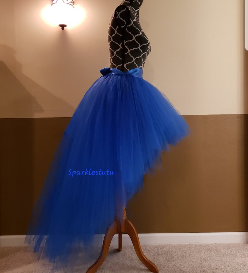 Puede incluir: Falda de tul azul real alta-baja con una faja de sat&eacute;n. La falda est&aacute; en un maniqu&iacute; y la cola de la falda est&aacute; arrastrando en el suelo. El texto "Sparkles tutu" es visible en la falda.