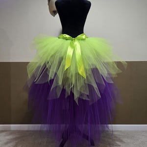 Peut inclure: Jupe tutu à plusieurs épaisseurs en tulle vert citron et violet, présentée sur un mannequin noir. La jupe est nouée avec un ruban de satin vert citron. Conçue pour les costumes ou la danse.