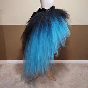 May include: A black and blue tutu skirt displayed on a mannequin. The skirt features a black waistband and a layered design that fades from black to a vibrant blue. The tulle skirt is designed to be asymmetrical, with a longer length in the back.