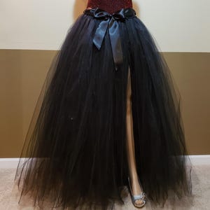 May include: A black tulle skirt with a front slit and a black satin bow at the waist.