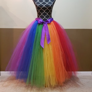 Könnte beinhalten: Ein Regenbogen-Tüllrock mit einer violetten Schleife aus Satin. Der Rock ist voll und fließend, und die Farben sind leuchtend.