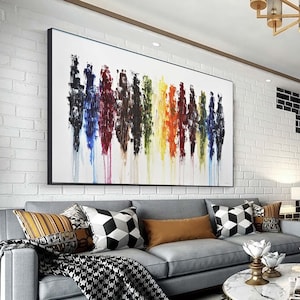 May include: Abstract painting with vertical stripes of various colors, including red, blue, yellow, green, and black. The painting is framed in black and hangs on a white brick wall above a gray sofa.