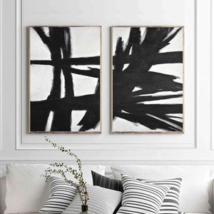May include: Two black and white abstract paintings with bold brushstrokes. The paintings are framed in a simple, modern style.