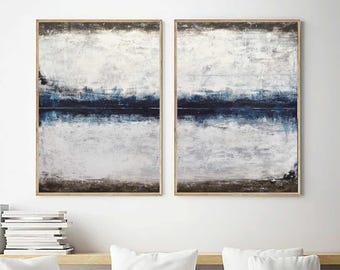 May include: Two abstract paintings with a white background and a dark blue horizontal line in the middle. The paintings are framed in a light wood frame.