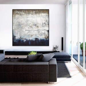 May include: A large abstract painting in shades of blue, grey, and white hangs on a white wall above a black sofa in a modern living room.